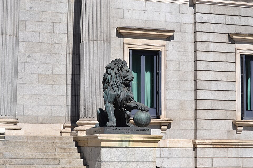 León de bronce en primer plano ante las columnas del Congreso de los Diputados, en Madrid
